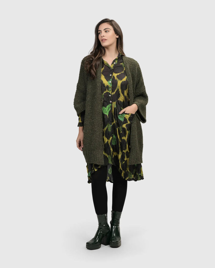 A woman donning a cozy ALEMBIKA Sunday Cardigan, Hunter green long knit cardigan dress and black boots.