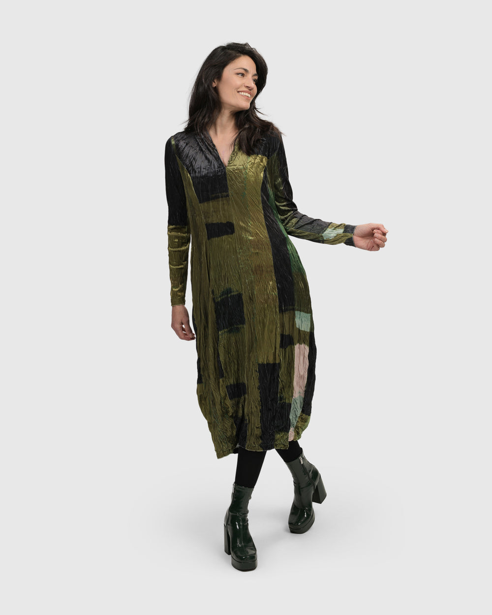 A woman wearing a green Al Fresco Cocoon Dress, Olive by ALEMBIKA and black boots.