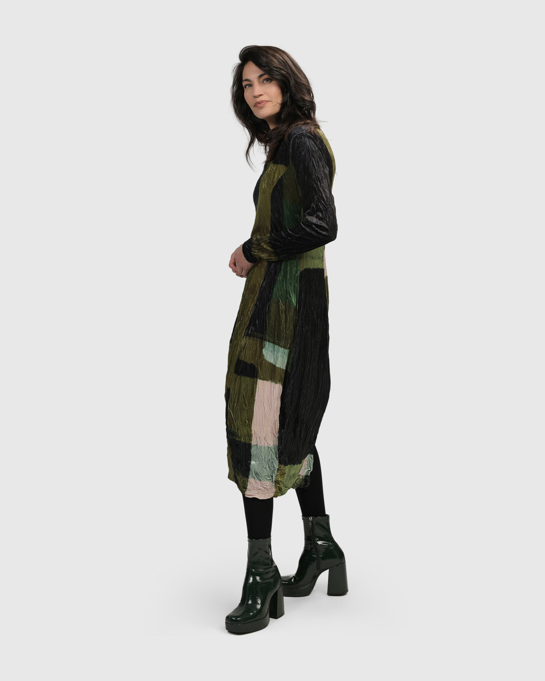 A woman wearing the ALEMBIKA Al Fresco Cocoon Dress in Olive, a knitted green and black dress that falls below-the-knee.