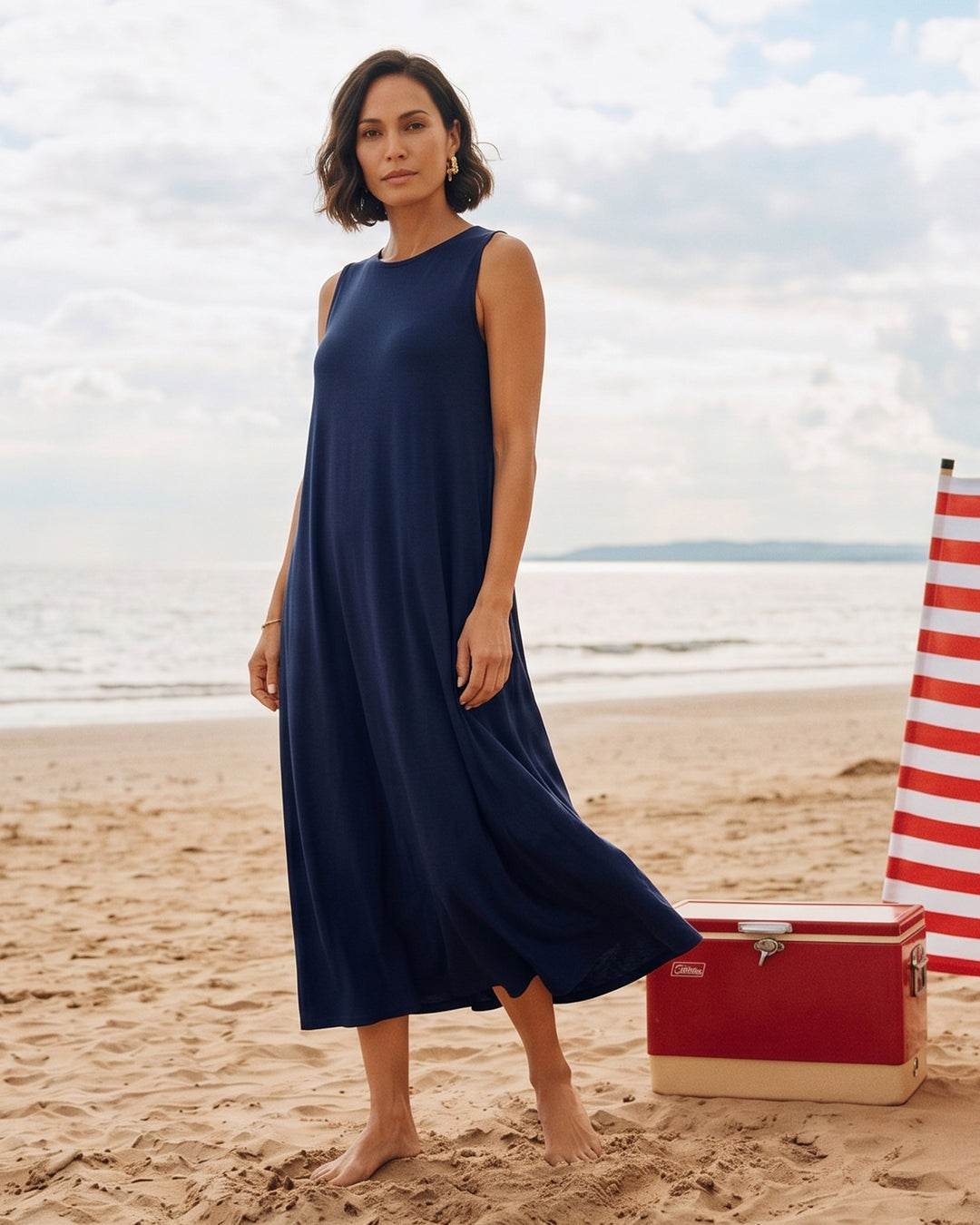 Woman in a blue dress standing on a beach with a cooler in the background