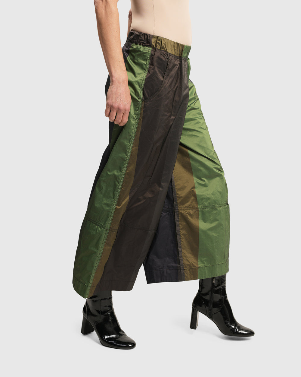 A woman stylishly dons the woven ALEMBIKA Alfresco Market Pants, Forest, featuring an elastic waistband and a captivating forest colored palette.