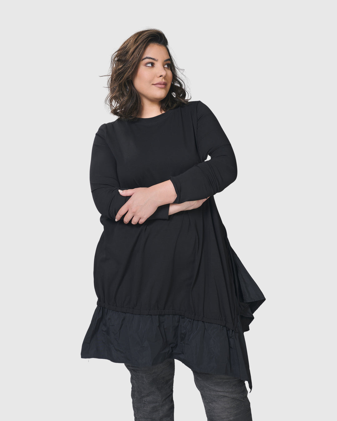 A woman wearing an ALEMBIKA Urban New Wave Tunic Top in Black with ruffles and long sleeves.