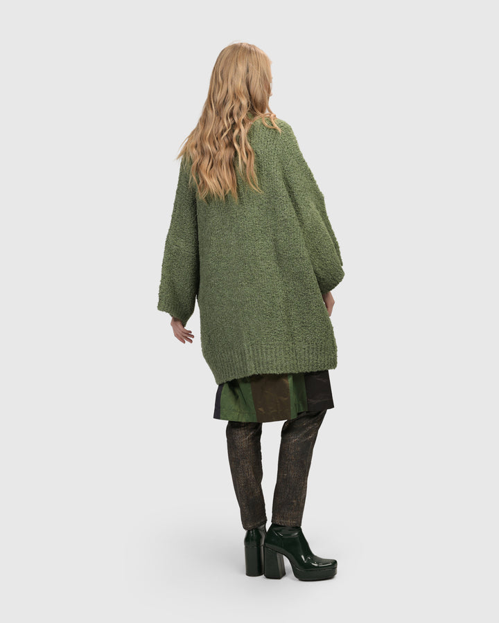 The back view of a cozy woman in the ALEMBIKA Sunday Cardigan, Green, perfect for layering.