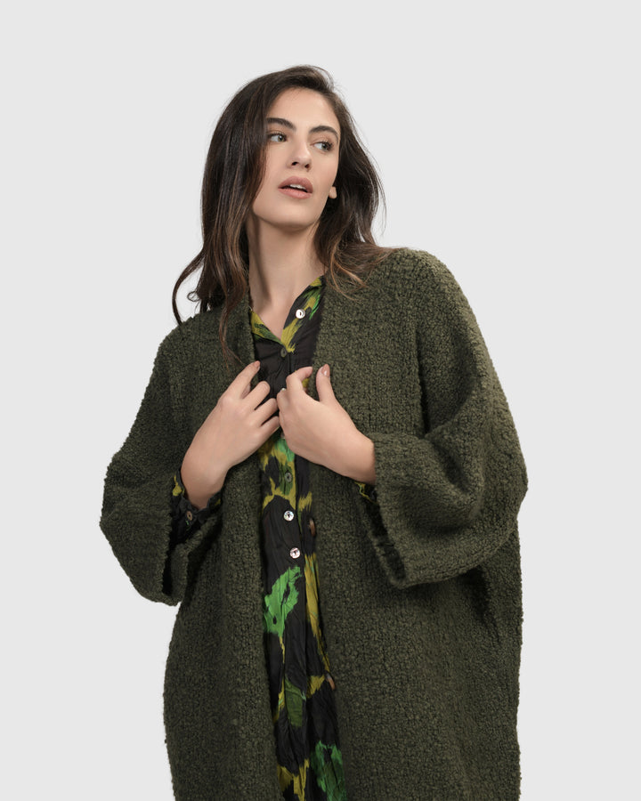 The model is wearing a Sunday Cardigan in hunter green from ALEMBIKA.
