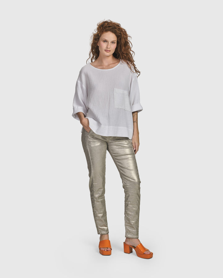 A woman wearing a white top and Iconic Stretch Jeans, Metallic Luster pants with a drawstring stretch waist from ALEMBIKA.