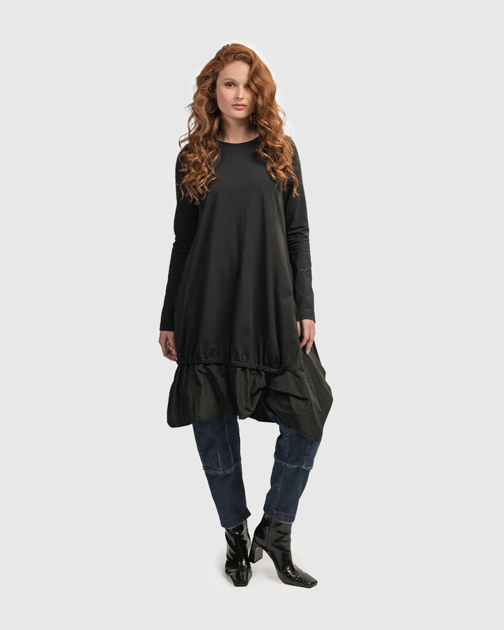 A woman wearing an ALEMBIKA Urban New Wave Tunic Top in Black, with ruffles and a scoop neck.