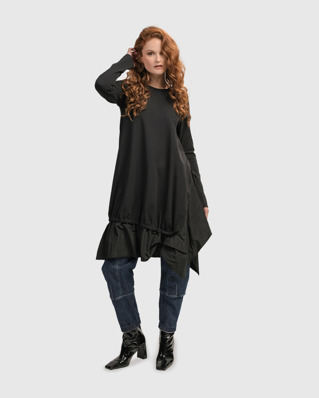 A woman wearing an ALEMBIKA Urban New Wave Tunic Top in Black with ruffles has a scoop neck and long sleeves.