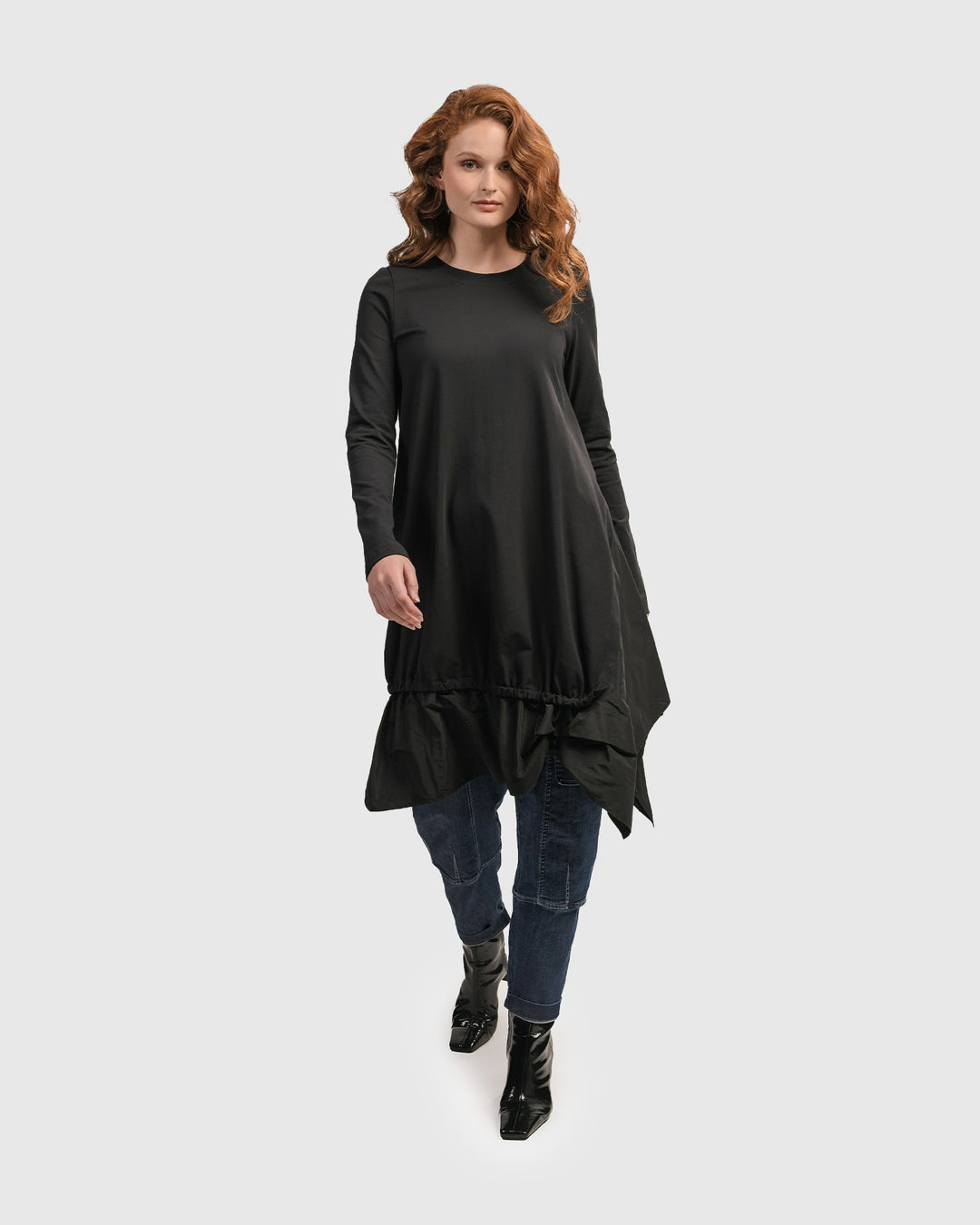 A woman wearing the ALEMBIKA Urban New Wave Tunic Top in Black with a ruffled hem and long sleeves.