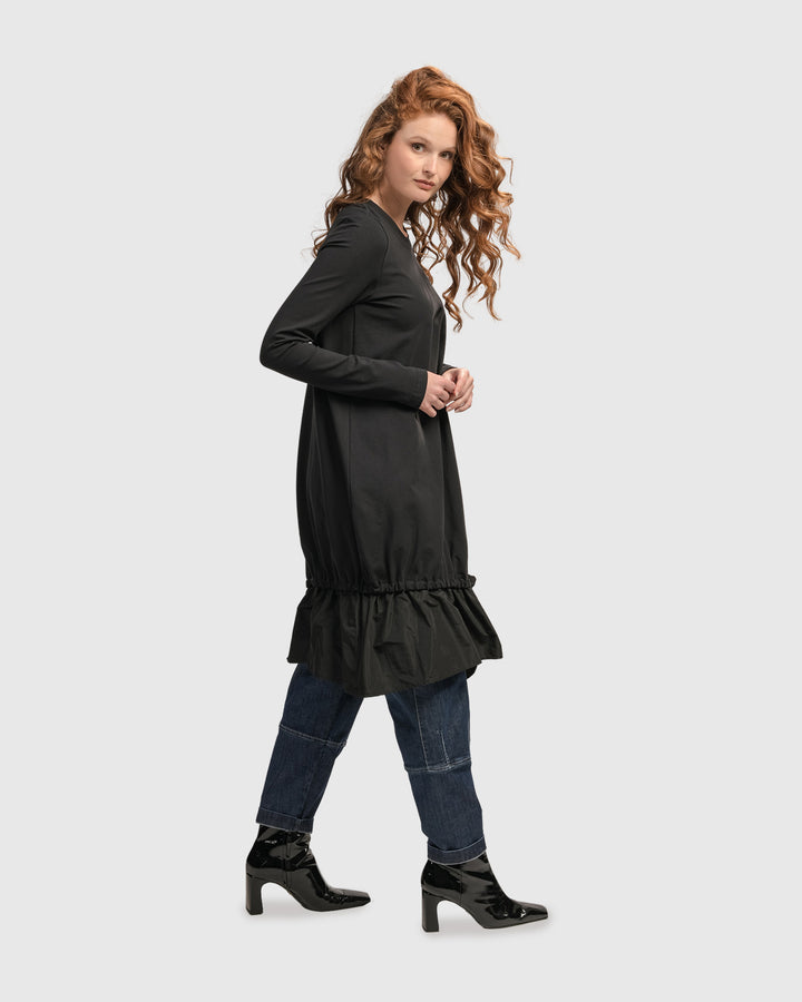 A woman wearing an ALEMBIKA Urban New Wave Tunic Top, Black with a ruffled hem and nylon skirting.